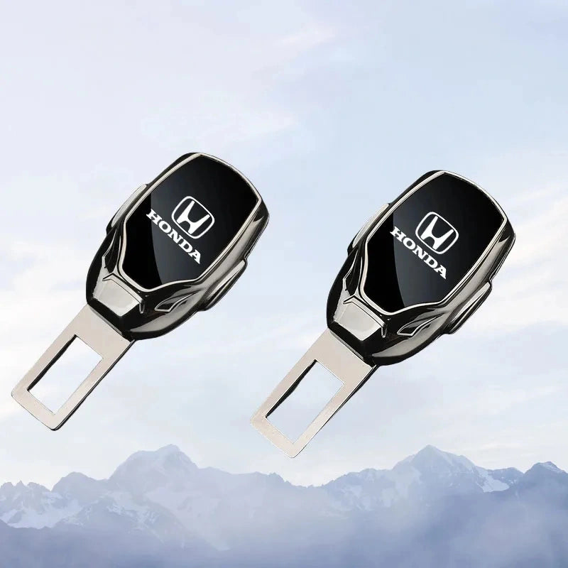 Two black and silver Honda seat belt quick-release locks with the Honda logo, shown against a light blue sky and mountain background.