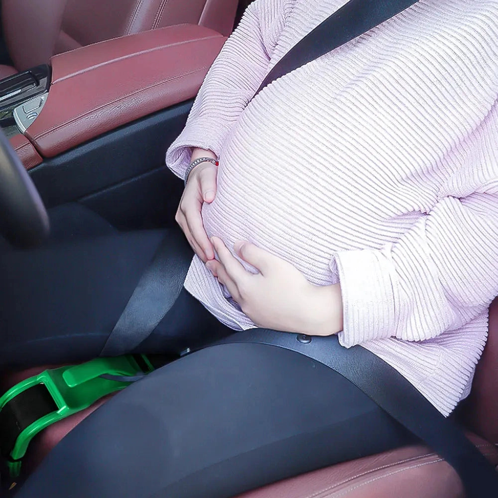 Pregnant woman wearing a light pink sweater sitting in a car with a green bump seat belt adjuster positioning the lap belt safely below her belly.
